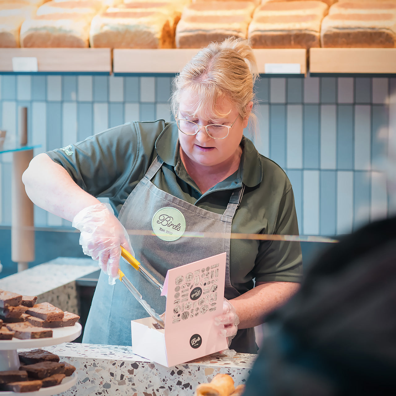 A baker putting sweet treats into a Birds Bakery box