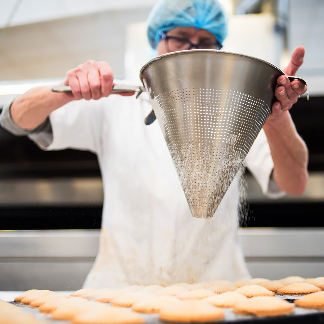 Baker shaking sugar on top of cookies