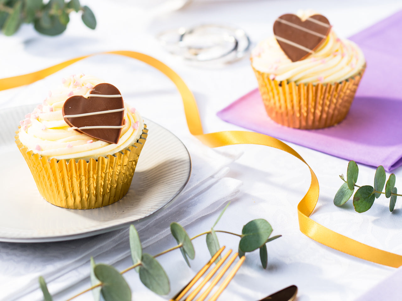 Two cupcakes with chocolate hearts in a gold foil case