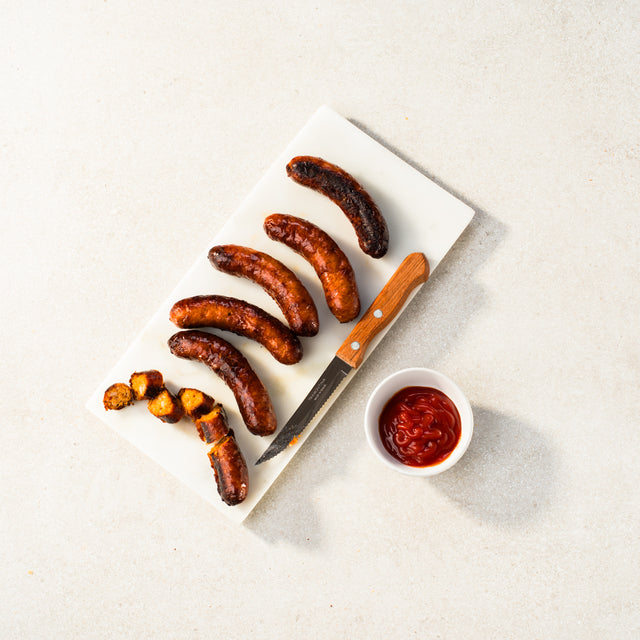 Pork and tomato sausages on a chopping board with tomato sauce